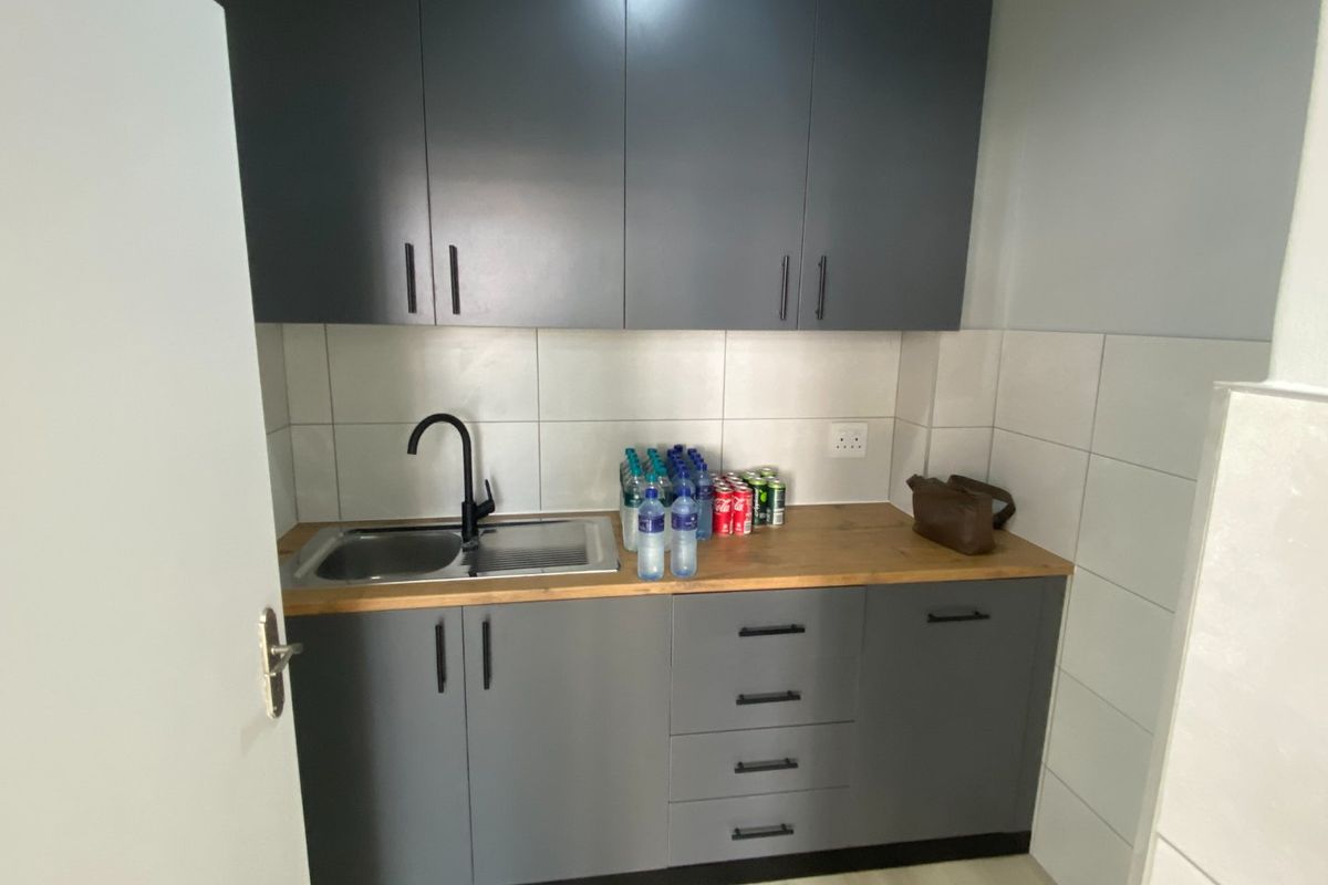 A compact kitchenette featuring modern grey cabinetry, a wooden countertop, a stainless steel sink with a black faucet, and tiled splashbacks.