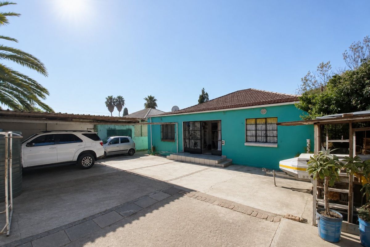 Rear exterior view of the property featuring a concrete driveway, carport, and tiled roof with security features on windows and doors.