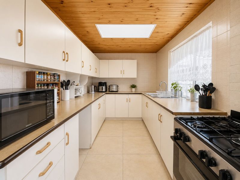 A functional U-shaped kitchen featuring white cabinetry, laminate countertops, a gas stove, and a timber-clad ceiling with a central skylight.