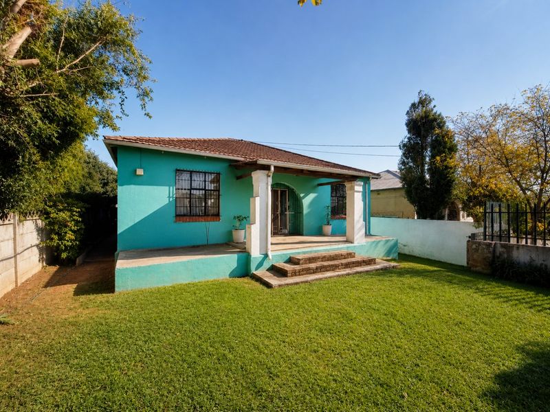 Rear view of a detached house featuring a covered patio, brick steps, and a spacious garden with a boundary wall.