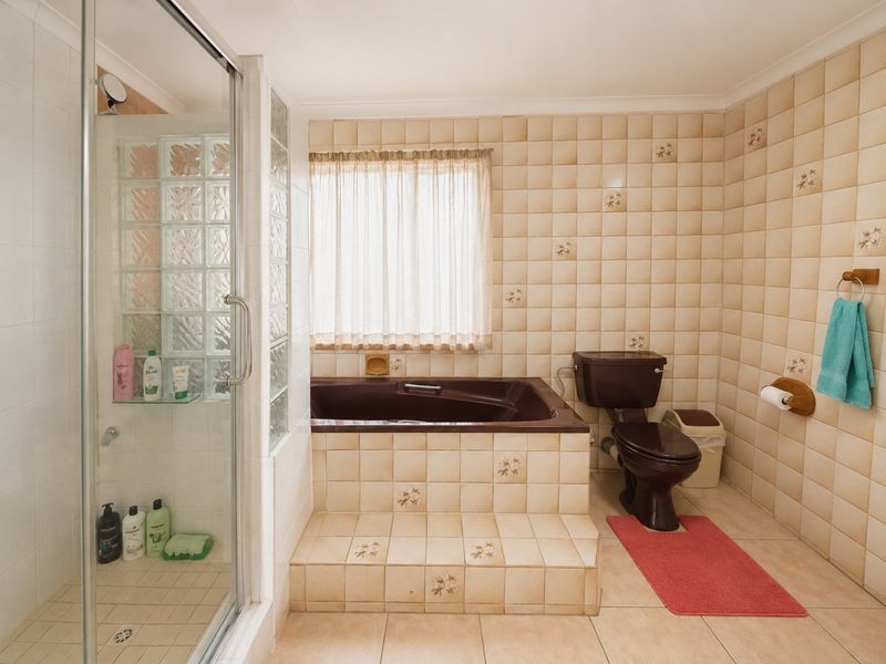 A dated bathroom featuring a built-in bathtub, glass shower enclosure, and ceramic tiling throughout. The space offers a functional layout ready for modern updates.