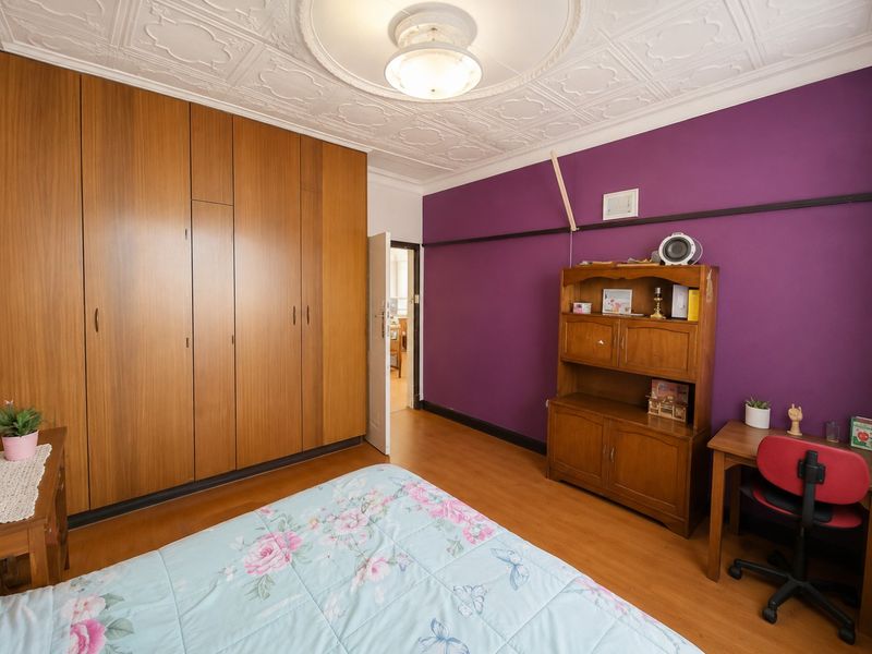 Bedroom featuring built-in wooden wardrobes, laminate flooring, and a decorative pressed metal ceiling, offering a classic architectural foundation for potential updates.