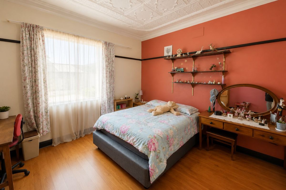 A bedroom featuring an ornate pressed metal ceiling, laminate timber flooring, and a distinctive feature wall with built-in shelving.