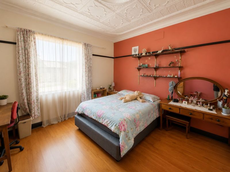 A bedroom featuring an ornate pressed metal ceiling, laminate timber flooring, and a distinctive feature wall with built-in shelving.