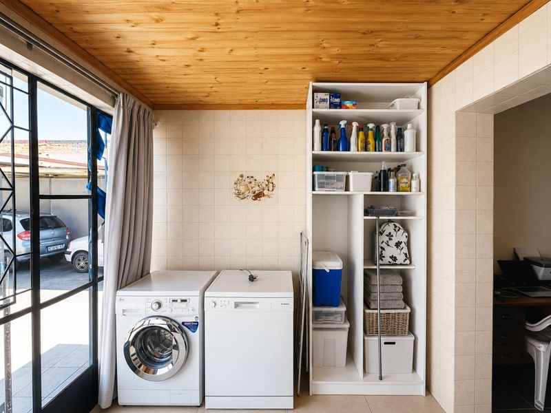 A functional laundry area featuring built-in shelving, tiled wall finishes, a timber ceiling, and direct access to the exterior via a sliding glass door.