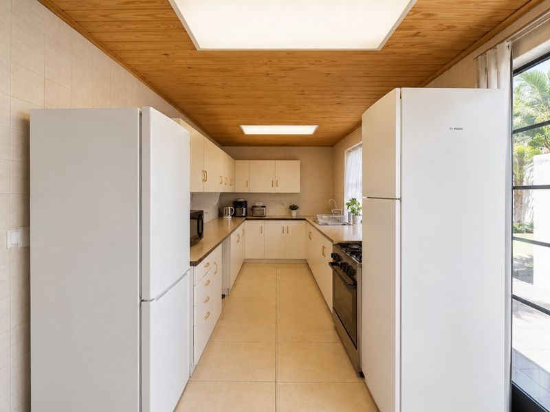 A functional galley-style kitchen featuring ample cabinetry, tiled flooring, a gas stove, and a distinctive timber-paneled ceiling with recessed lighting.