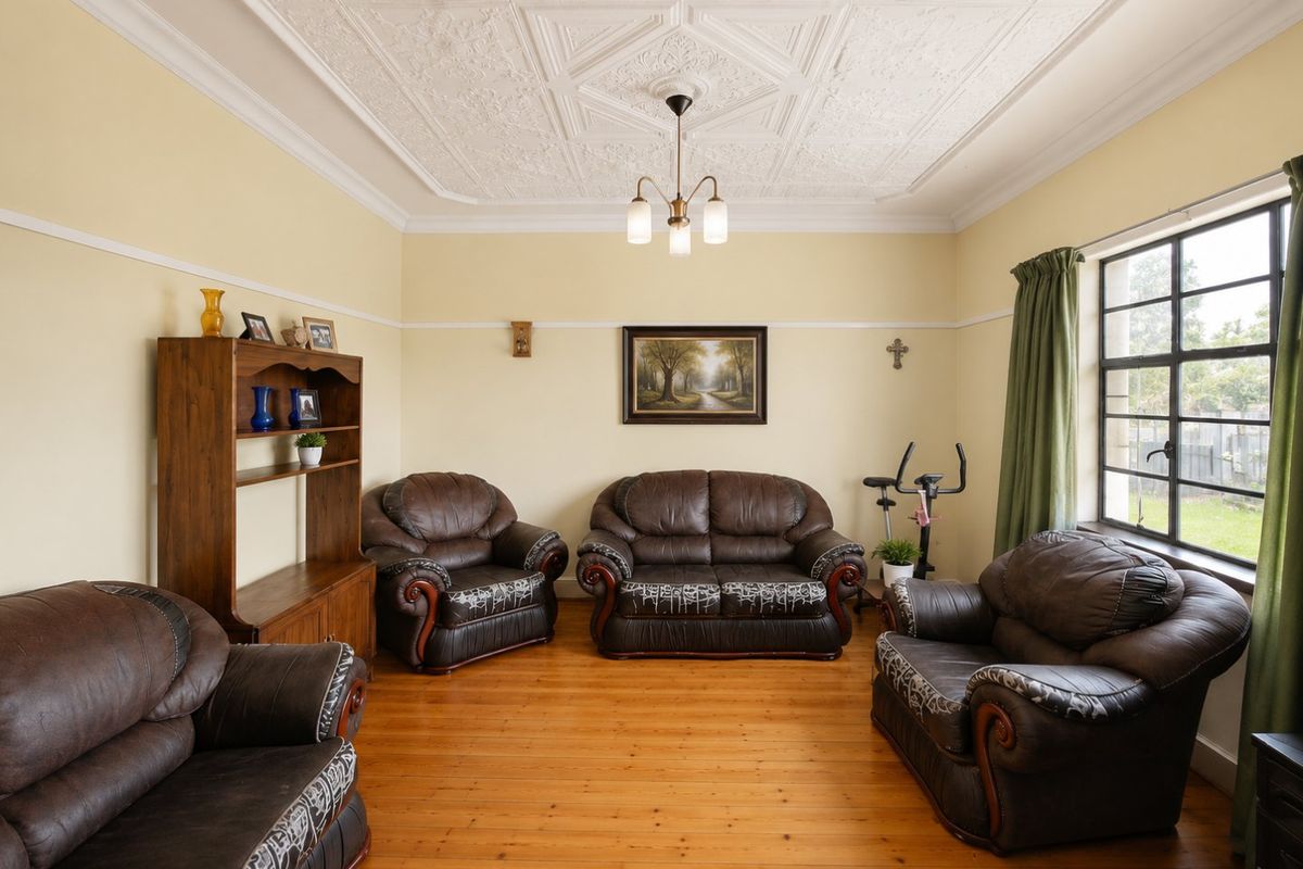 A spacious living room featuring original pressed metal ceilings, a decorative ceiling rose, timber flooring, and large steel-framed windows providing natural light.