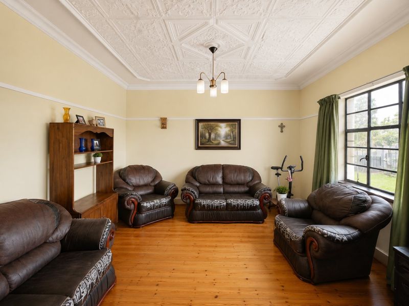 A spacious living room featuring original pressed metal ceilings, a decorative ceiling rose, timber flooring, and large steel-framed windows providing natural light.