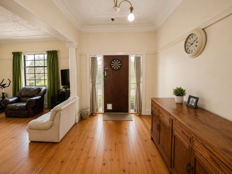 Welcoming entrance hall featuring polished timber flooring, decorative ceiling detailing, and a classic column, leading into an open-plan living area.