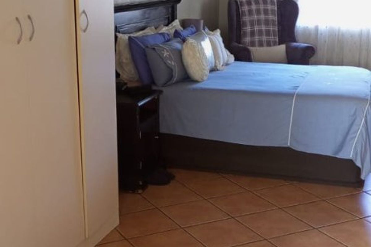 A bedroom featuring tiled flooring and built-in cupboards, offering a functional space with natural light.