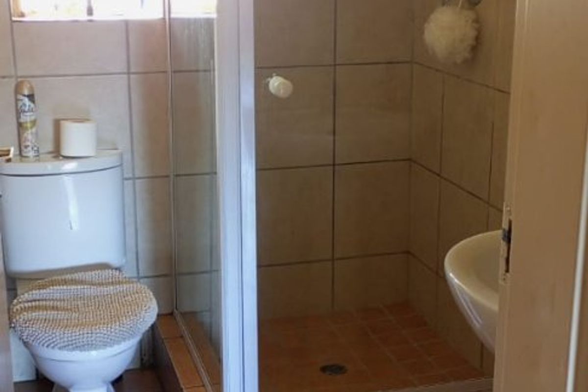 A functional bathroom featuring a tiled shower enclosure, toilet, and basin with neutral wall and floor tiling.