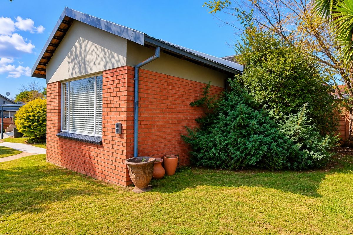 A view of the side and rear brick facade of the house, featuring a pitched roof, downpipe, and a window with fitted blinds.