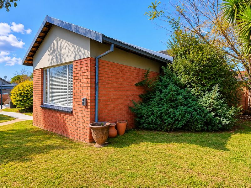 A view of the side and rear brick facade of the house, featuring a pitched roof, downpipe, and a window with fitted blinds.