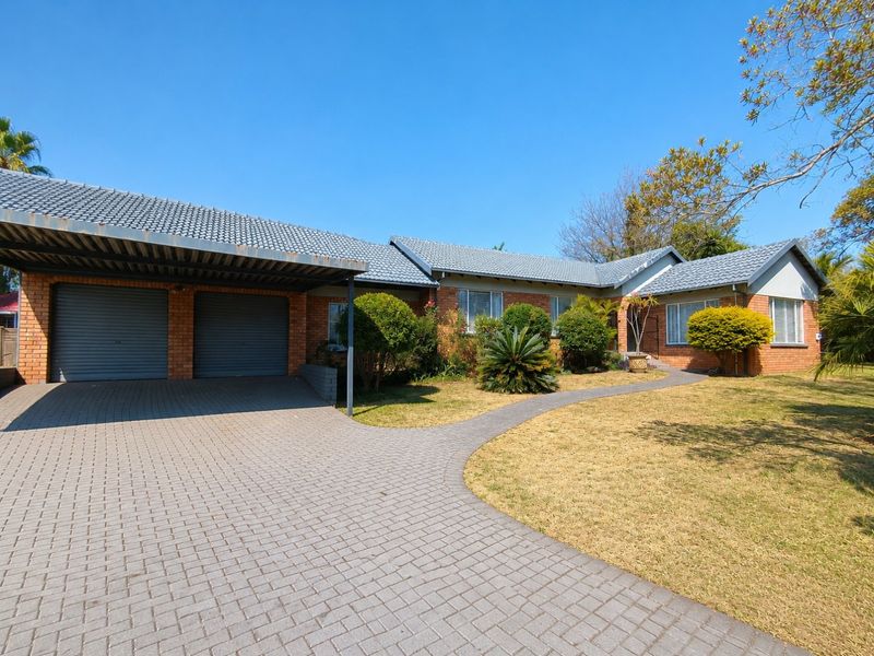 Front view of a single-story brick house featuring a double garage, paved driveway, and a landscaped front garden with a paved walkway.