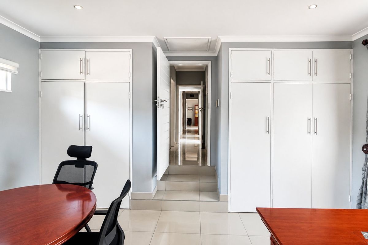 A well-maintained bedroom featuring extensive built-in cupboards, neutral tiled flooring, recessed lighting, and direct access to a hallway.
