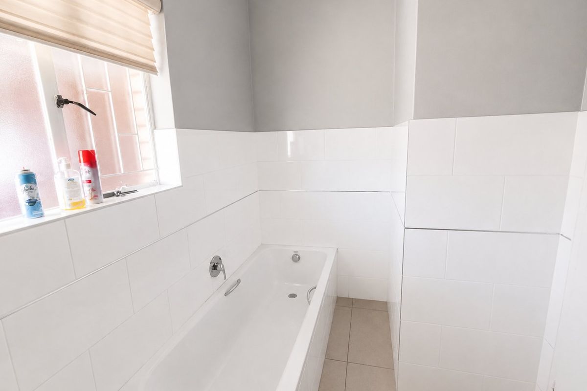 A clean and modern bathroom featuring a built-in bathtub, neutral wall and floor tiling, and a window providing natural light.