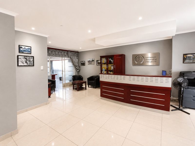 A professional office reception area featuring tiled flooring, recessed lighting, and a built-in reception desk, leading to an adjacent workspace.