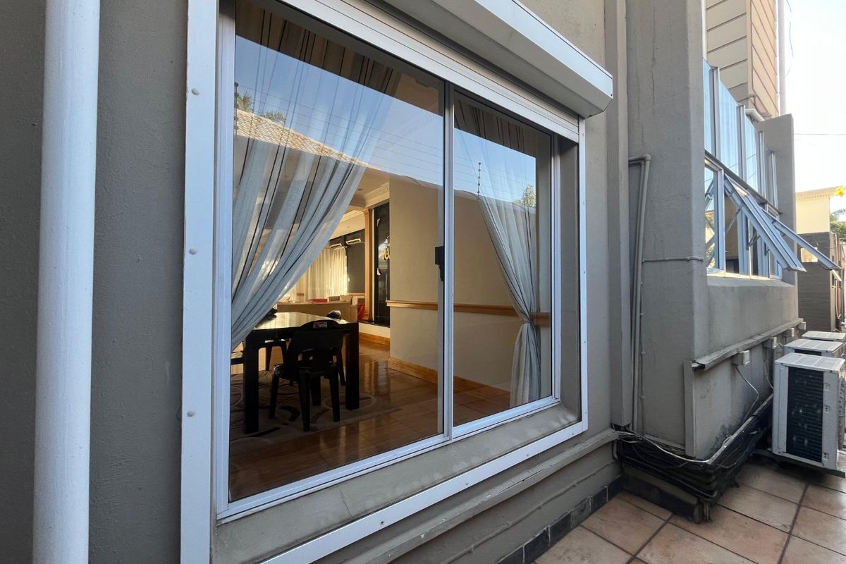 Exterior view of the rear facade featuring a large sliding window with an integrated roller shutter and tiled patio area.