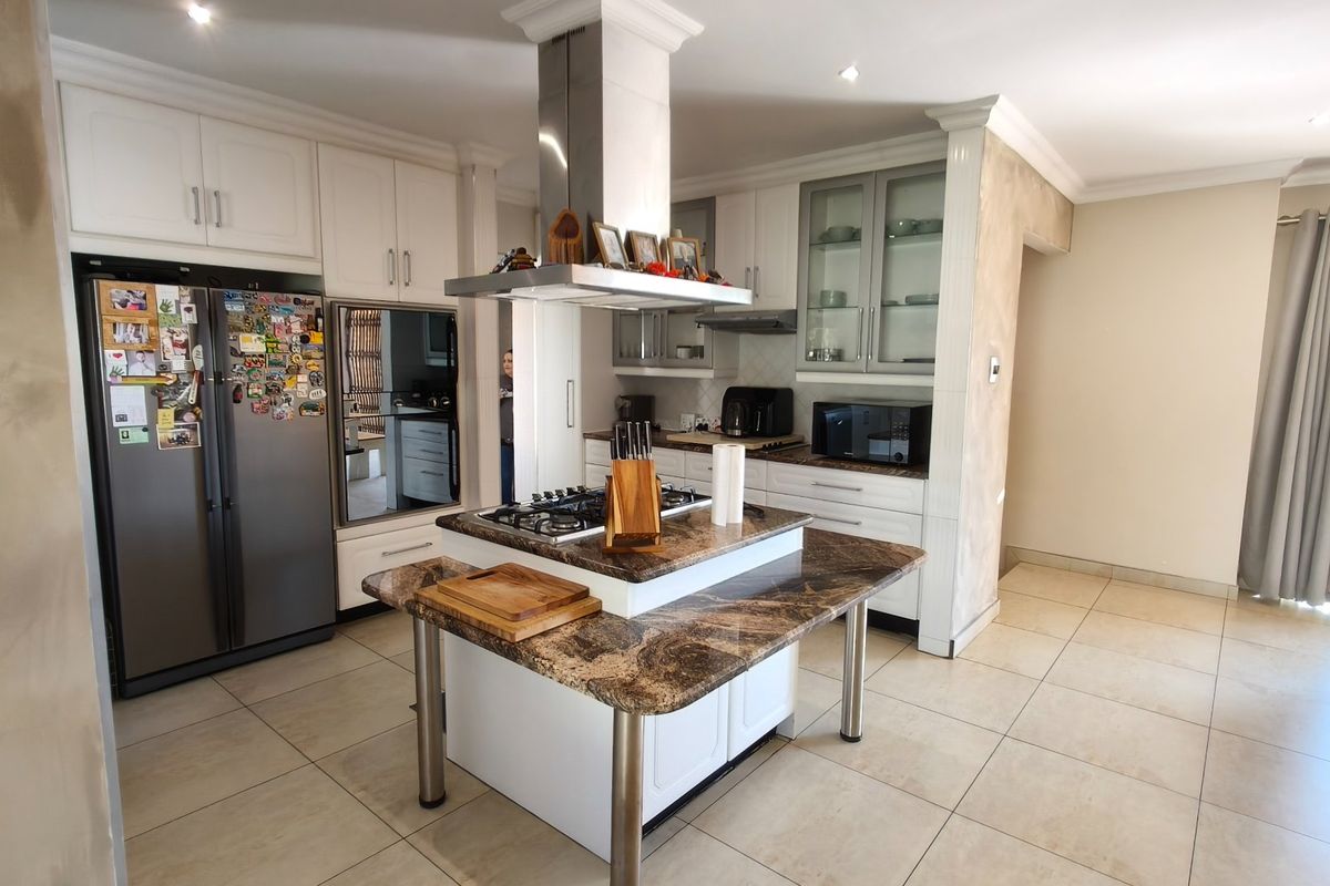 A well-appointed kitchen featuring a central island with a gas hob, granite countertops, and ample white cabinetry with integrated storage solutions.