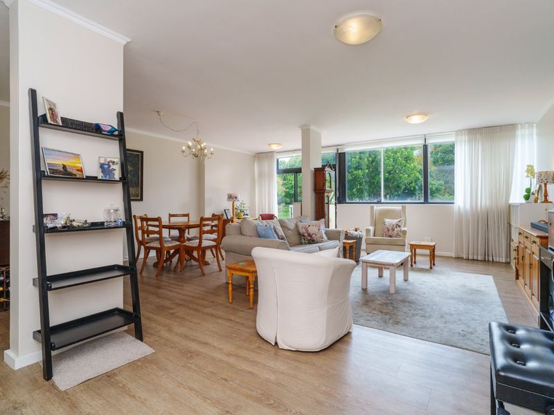 Spacious open-plan living and dining area featuring light-toned laminate flooring, large windows providing natural light, and neutral wall finishes.