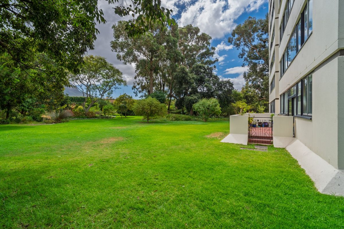 A view of the apartment building's rear facade featuring a well-maintained lawn and landscaped garden area with direct access via a security gate.