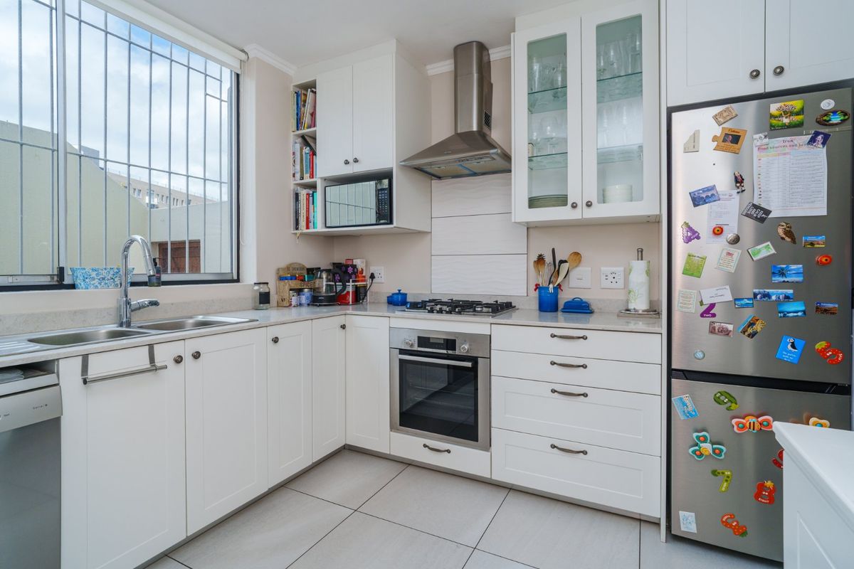 A well-maintained kitchen featuring white cabinetry, stone countertops, stainless steel appliances, and tiled flooring, offering a clean and functional cooking space.