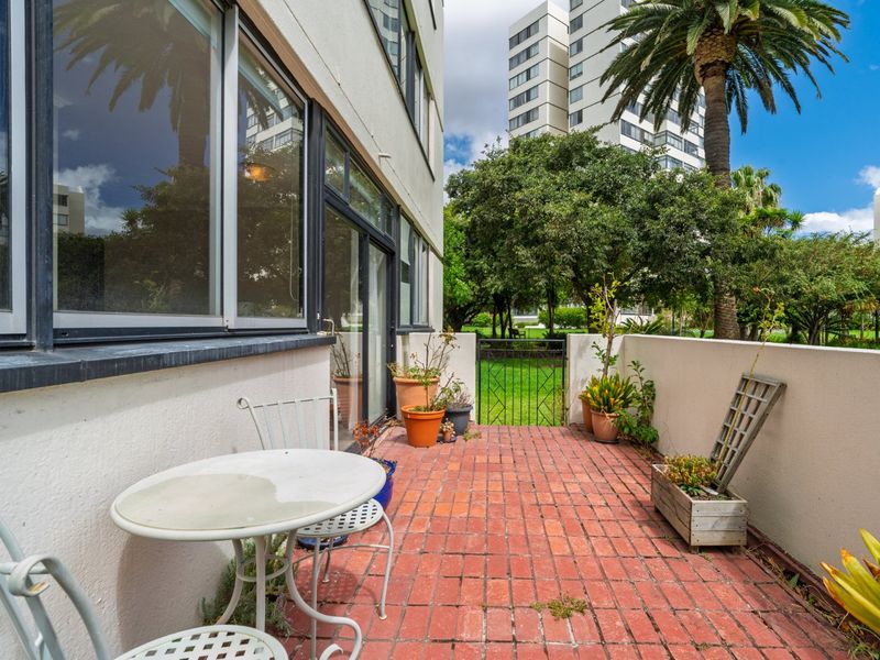 A ground-floor patio featuring red brick paving, a metal gate providing garden access, and sliding glass door access to the apartment interior.