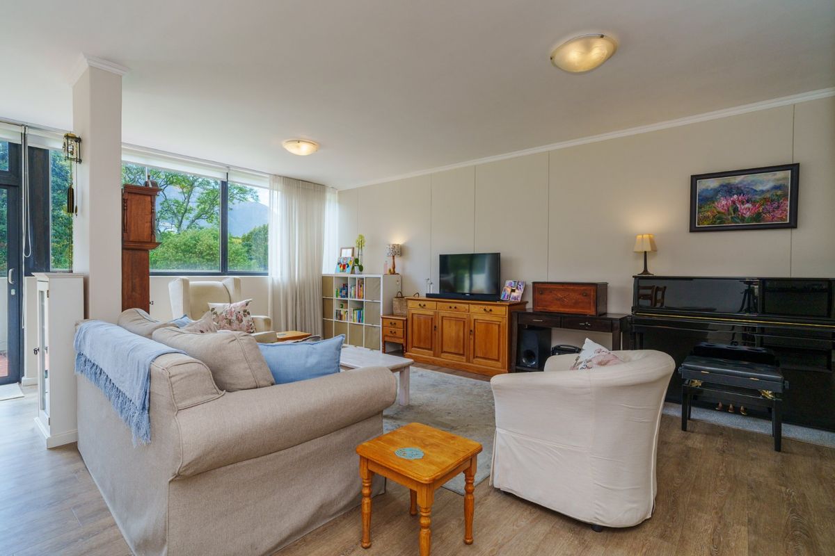 A spacious and bright living room featuring large windows with natural light, laminate flooring, and neutral wall finishes.