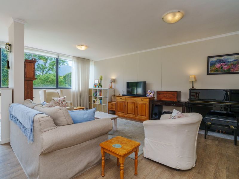 A spacious and bright living room featuring large windows with natural light, laminate flooring, and neutral wall finishes.
