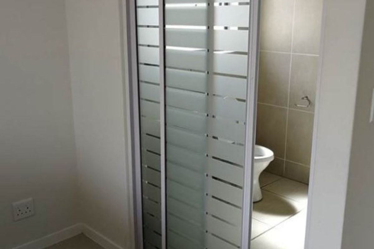 A clean, modern bathroom featuring a sliding frosted glass door, neutral ceramic floor and wall tiling, and a standard toilet.