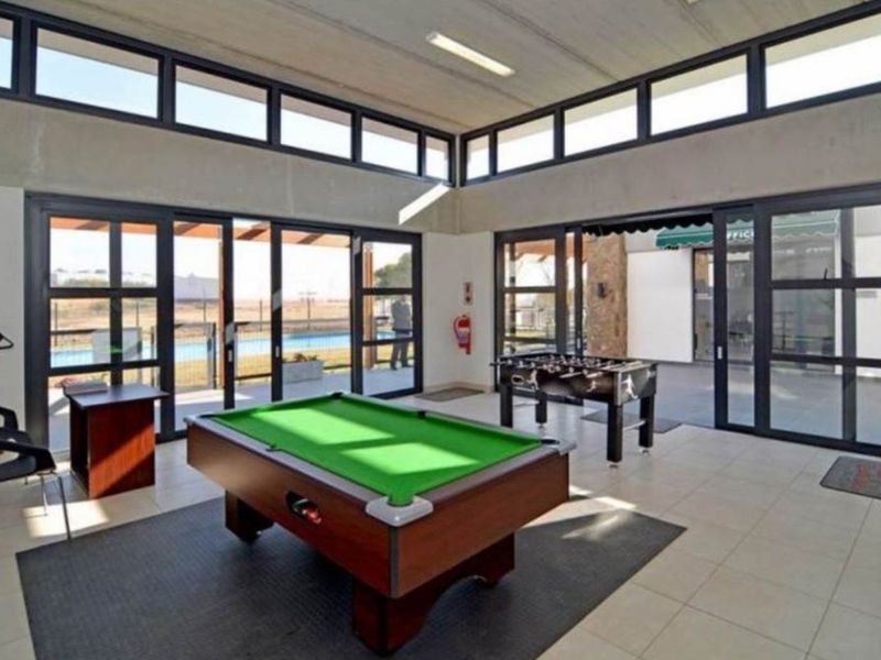 A spacious clubhouse area featuring large glass sliding doors, clerestory windows for natural light, tiled flooring, and an exposed concrete ceiling.