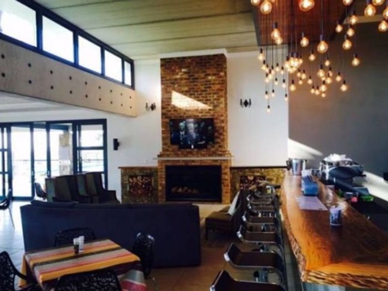 Spacious open-plan living area featuring a prominent brick fireplace, exposed beam ceilings, large windows, and a unique live-edge wood bar counter with pendant lighting.