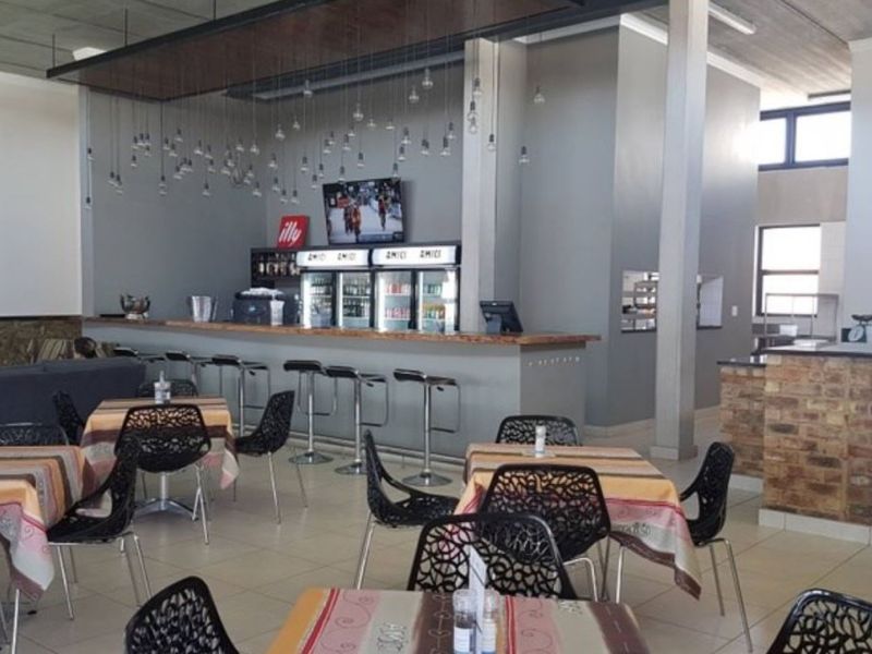 A spacious bar and dining area featuring a built-in bar counter, commercial refrigeration, and a traditional brick pizza oven.