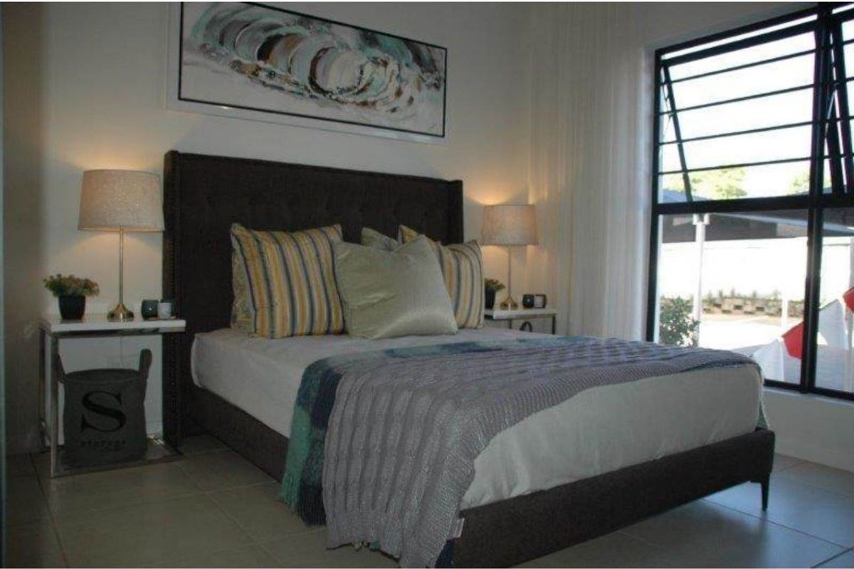 A well-lit bedroom featuring tiled flooring and a large top-hung window with security bars, providing natural light and ventilation.
