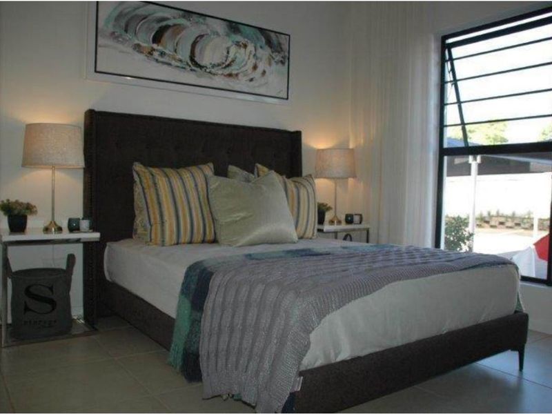 A well-lit bedroom featuring tiled flooring and a large top-hung window with security bars, providing natural light and ventilation.