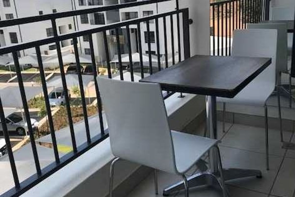 A private balcony featuring tiled flooring and a metal balustrade, offering an elevated view of the surrounding apartment complex.