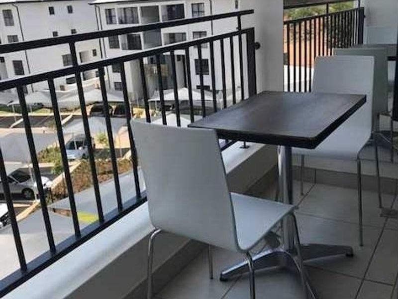 A private balcony featuring tiled flooring and a metal balustrade, offering an elevated view of the surrounding apartment complex.