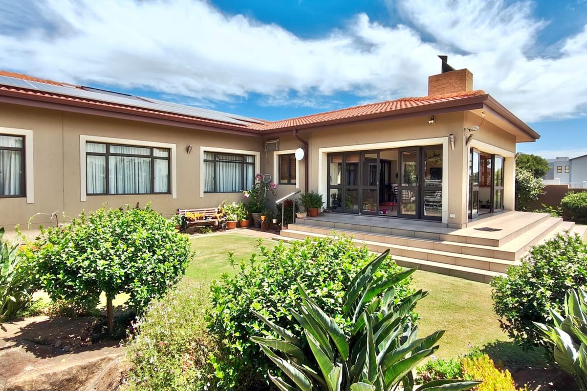 A well-maintained rear exterior view featuring a tiled patio, sliding glass doors, brick chimney, and solar panels overlooking a landscaped garden.