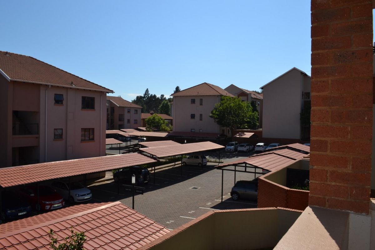 An elevated view of the apartment complex grounds, featuring paved parking areas with covered carports and surrounding residential building blocks.