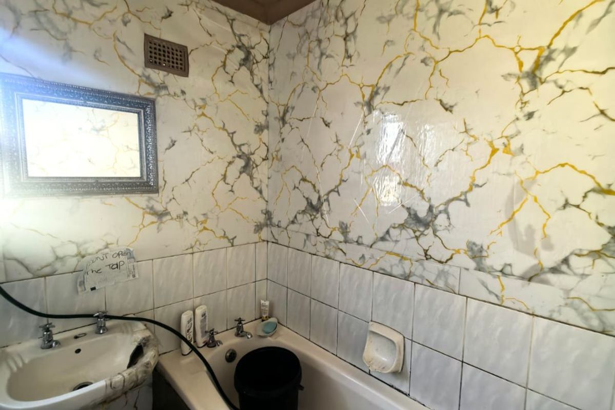 A dated bathroom featuring a pedestal washbasin and bathtub with marble-effect wall tiling, requiring significant renovation and modernization of fixtures and finishes.