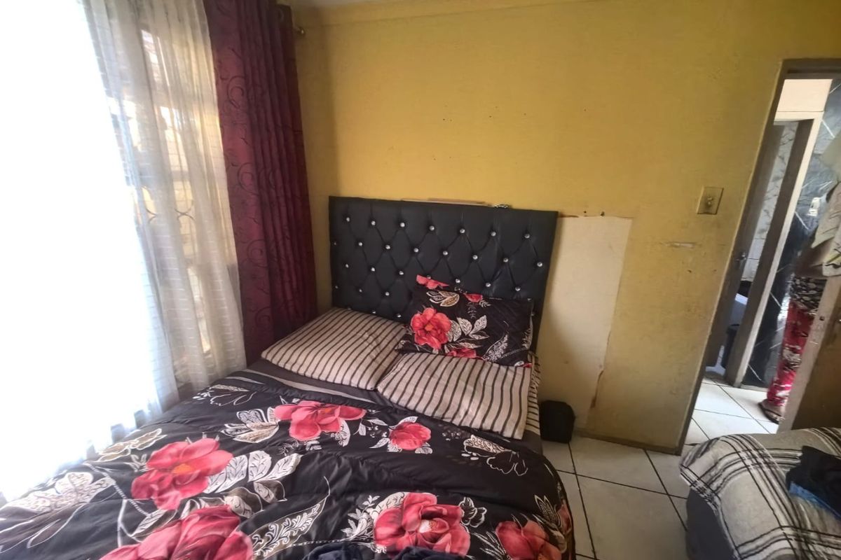 A bedroom featuring tiled flooring and yellow walls, currently showing signs of wear and damage to the wall finish.