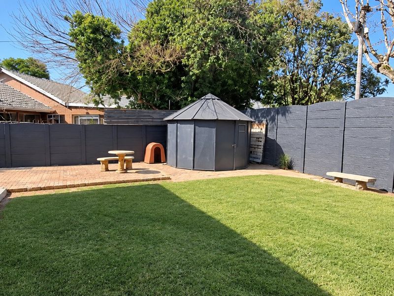 A well-maintained rear garden featuring a paved patio area, manicured lawn, and secure boundary walling with a garden shed.