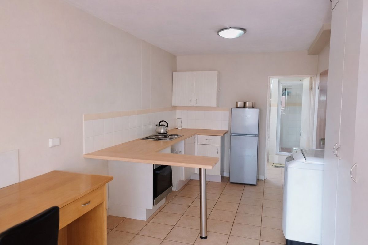 Compact kitchen featuring light-toned cabinetry, laminate countertops, tiled splashback, and ceramic flooring, with an integrated oven and hob setup.