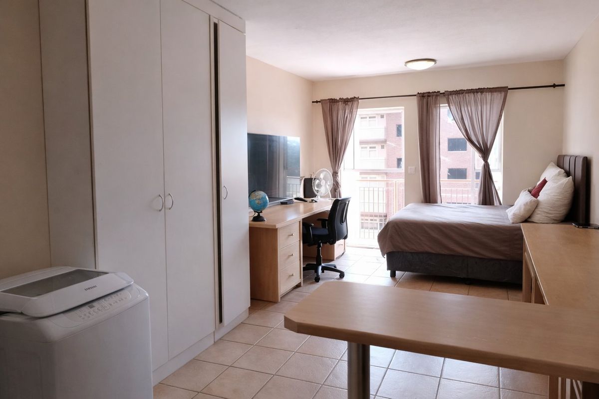 A functional bedroom featuring built-in cupboards, tiled flooring, and direct access to a balcony, providing natural light and ventilation.