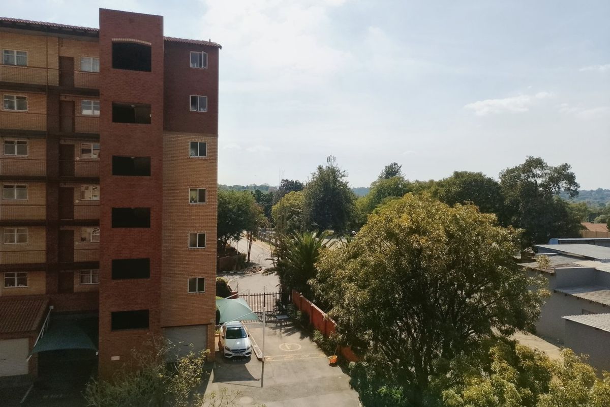 An elevated view of the apartment building exterior, showing the brick facade, paved driveway area, and surrounding mature trees.