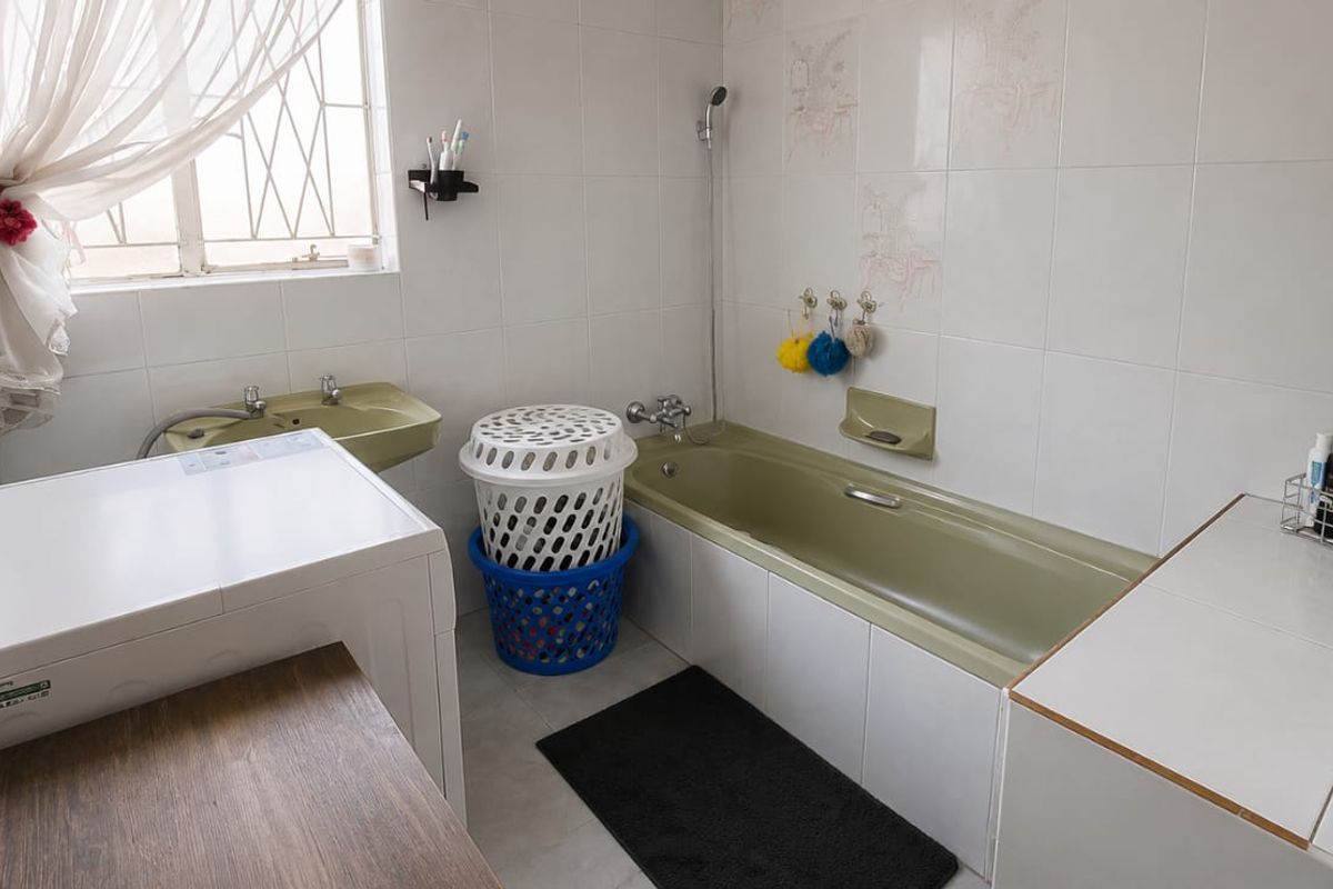 A functional bathroom featuring a bathtub, basin, and full-height wall tiling, with security bars on the window.
