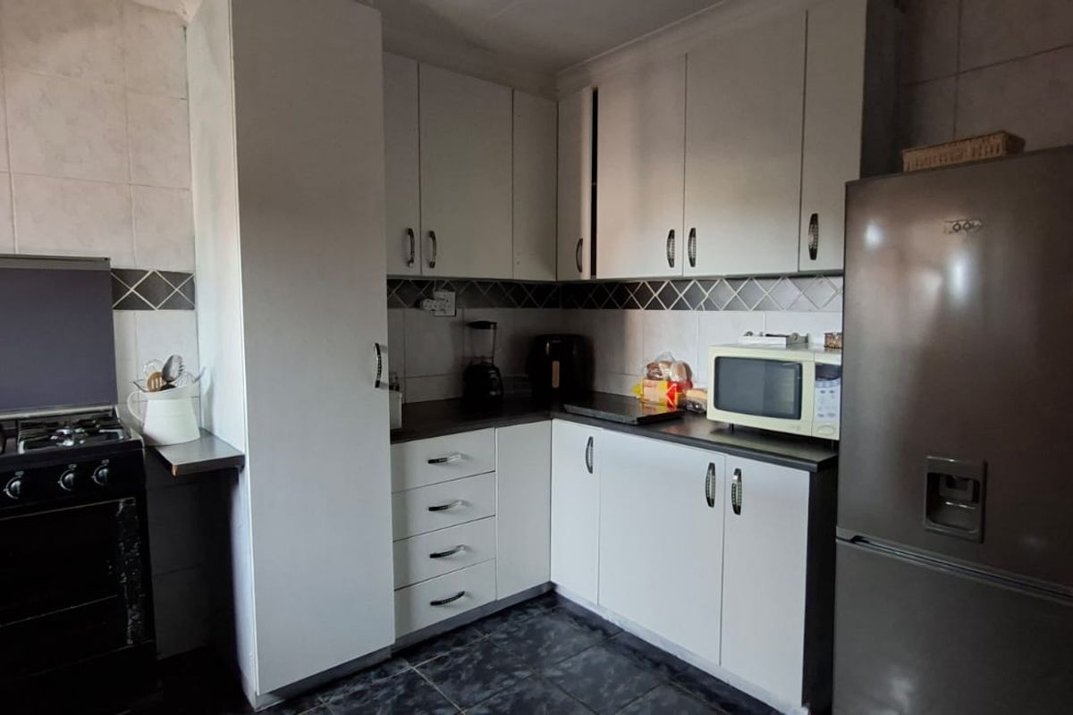 A functional kitchen featuring built-in cabinetry, a gas stove, tiled backsplash, and dark tiled flooring, offering a practical layout for daily meal preparation.