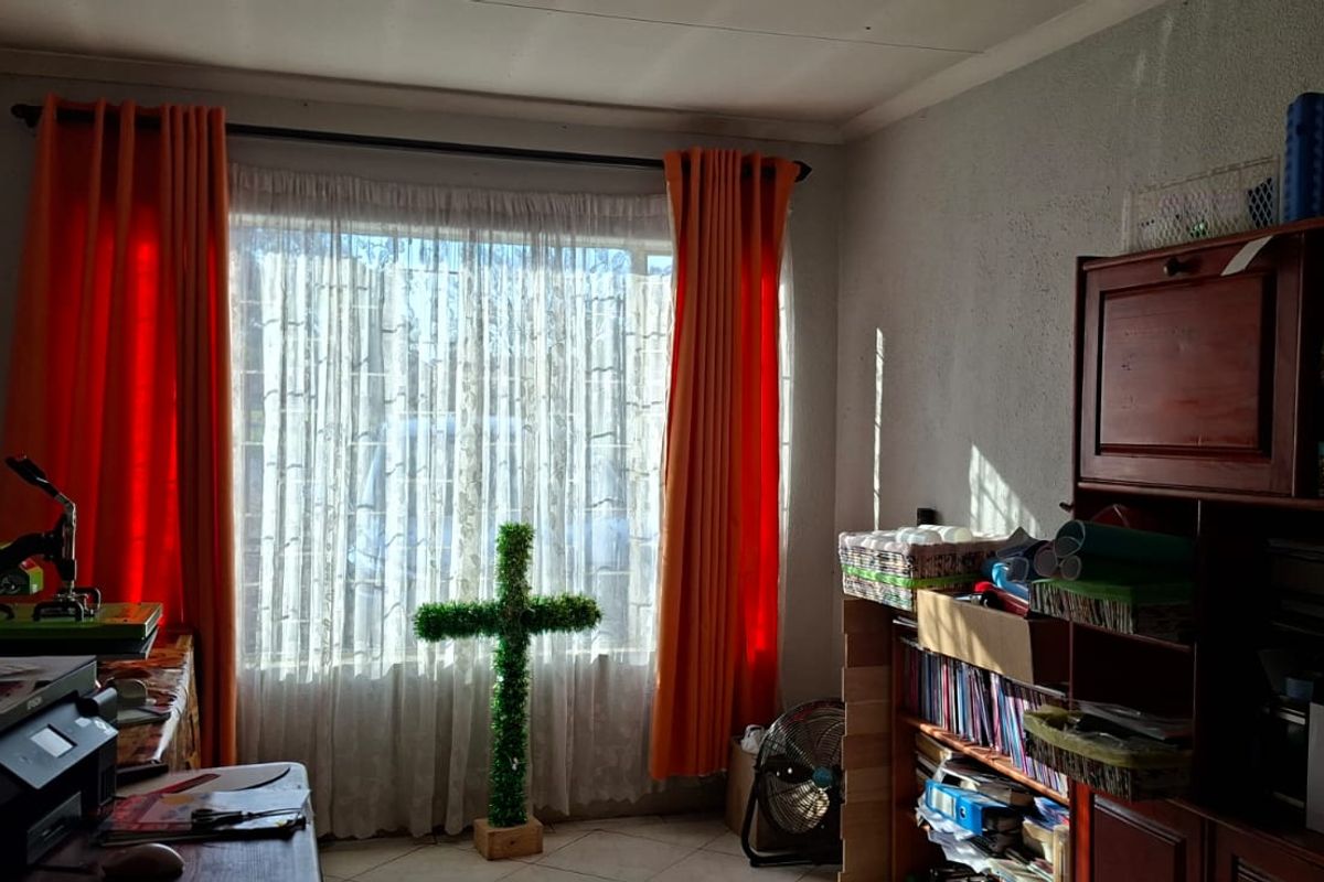 A bedroom featuring tiled flooring and large windows with curtain rails, offering a functional space with natural light.