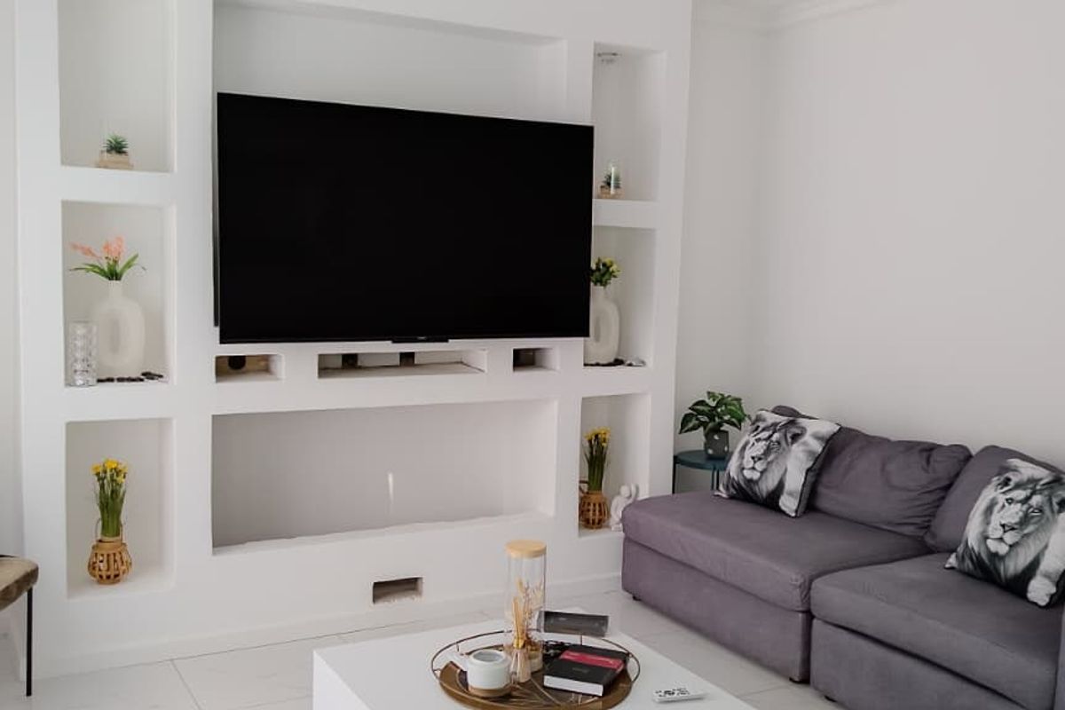 A bright living room featuring a custom built-in white media wall with integrated shelving and a central television mount.