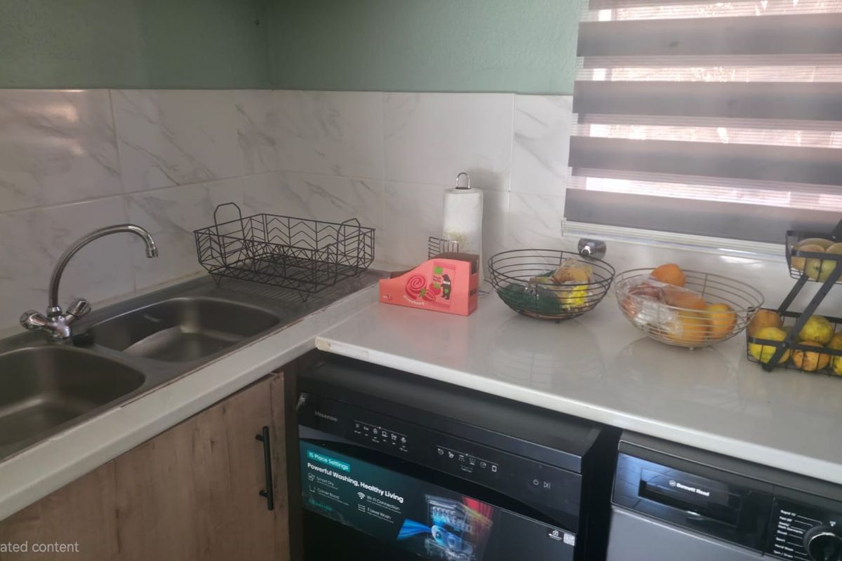 A functional kitchen area featuring a double bowl stainless steel sink, marble-look tile splashback, and integrated dishwasher with ample countertop workspace.
